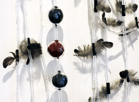 Detail of a necklace made of long, cylindrical glass, feathers, and glass spheres in a row that are filled with dark blue and red material.